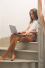 Mulher bonita usando laptop nas escadas em casa — Fotografia de Stock