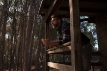 Thoughtful man with mobile phone standing at cabin porch — Stock Photo