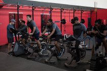Jóvenes atletas haciendo ejercicio en bicicletas estáticas en un gimnasio - foto de stock