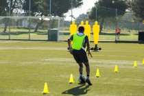Jogador de futebol driblando através de cones no campo esportivo — Fotografia de Stock