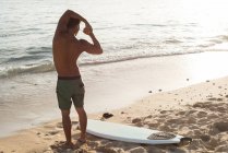 Vue arrière d'un surfeur masculin faisant de l'exercice sur la plage — Photo de stock