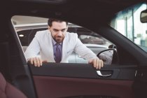 Retrato de vendedor confiante examinando carro no showroom — Fotografia de Stock