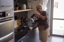 Старша жінка посміхається під час приготування кави на кухні вдома — стокове фото