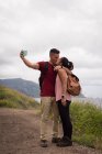 Coppia baciarsi mentre prende selfie con il telefono cellulare in campagna — Foto stock