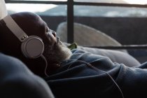 Старший чоловік розслабляється на дивані, слухаючи музику вдома — стокове фото