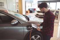 Vendedor de pie junto al coche y folleto de lectura fuera de la sala de exposición - foto de stock