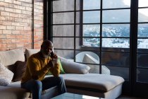 Senior man having coffee while talking on mobile phone at home — Stock Photo