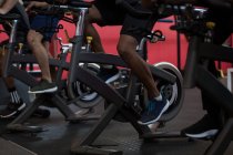Sección baja de atletas que hacen ejercicio en bicicletas estáticas en un gimnasio - foto de stock