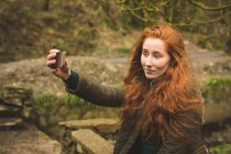 Hermosa excursionista femenina tomando selfie con teléfono móvil en el bosque - foto de stock