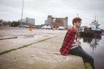 Nachdenklicher junger Mann sitzt am Hafen — Stockfoto