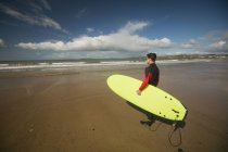 Серфер з дошкою для серфінгу дивиться на море з пляжу — стокове фото