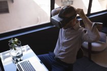 Uomo d'affari che utilizza cuffie realtà virtuale mentre lavora su laptop in ufficio — Foto stock