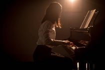 Вид сбоку на школьницу, играющую на фортепиано в музыкальной школе — стоковое фото