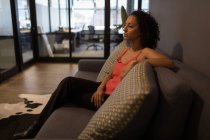 Задумчивая деловая женщина смотрит в сторону, сидя на диване в офисе — стоковое фото