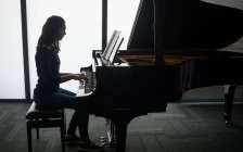 Vista lateral de la colegiala tocando el piano en la escuela de música - foto de stock