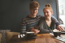 Jeune couple utilisant un téléphone portable dans un café — Photo de stock