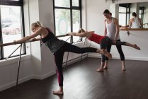 Trainer assisting young woman stretching on barre — Stock Photo