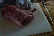 Sección media del carnicero cortando carne en la carnicería - foto de stock