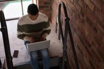 Внимательный человек, использующий ноутбук на лестнице дома — стоковое фото