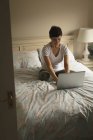 Mujer usando portátil en la cama en el dormitorio en casa - foto de stock