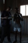 Entrenador y boxeador masculino interactuando sobre el portapapeles en el gimnasio - foto de stock