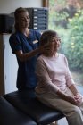 Fisioterapeuta dando un masaje a una mujer mayor en casa - foto de stock