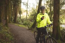 Young man with cycle using mobile phone in the forest — Stock Photo