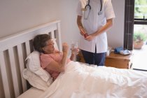 Physiotherapeutin gibt Seniorin zu Hause Medikamente — Stockfoto