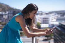 Donna d'affari appoggiata alla ringhiera durante l'utilizzo del telefono cellulare in una giornata di sole — Foto stock