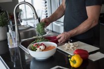 Мужчина моет овощи на кухне дома — стоковое фото