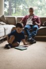 Батько і син, використовуючи цифровий планшет і мобільний телефон у вітальні на дому — стокове фото