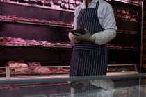Mid section of butcher using digital tablet in butcher shop — Stock Photo
