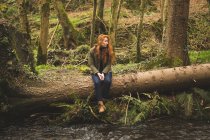 Красива жінка-пішохід, що сидить на стовбурі падіння біля річки — стокове фото