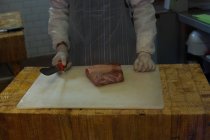 Sección media del carnicero de pie con trozo de carne en la carnicería - foto de stock