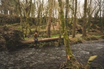 Joven excursionista sentada en el tronco caído del árbol cerca del río - foto de stock