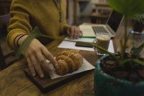 Seção média de jovem pegando um croissant enquanto trabalhava — Fotografia de Stock