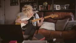 Молодая женщина играет на гитаре в гостиной дома — стоковое фото