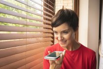 Жінка розмовляє по мобільному телефону біля вікна вдома — стокове фото