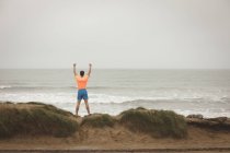Rückansicht eines Mannes, der mit erhobenen Händen am Ufer des Meeres steht — Stockfoto