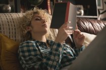 Mujer joven leyendo un libro en la sala de estar en casa - foto de stock