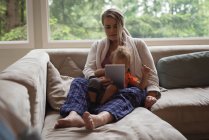 Мати і дитина сидять на дивані і використовують цифровий планшет вдома — стокове фото