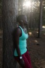 Erschöpfte Sportlerin lehnt im Wald an Baumstamm — Stockfoto