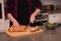 Donna che taglia un pezzo di pane in cucina a casa — Foto stock