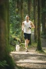 Uomo che fa jogging con il suo cane in una foresta lussureggiante — Foto stock