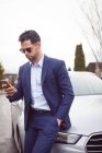 Uomo d'affari intelligente che utilizza il telefono cellulare vicino a un'auto — Foto stock