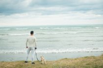 Vista trasera del hombre con su perro de pie en la orilla del mar - foto de stock
