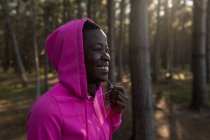Primo piano di atleta donna con giacca incappucciata sorridente nel bosco — Foto stock