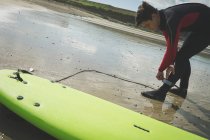 Серфер прикріплює дошку для серфінгу до ноги на пляжі — стокове фото