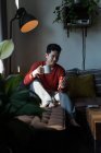 Мужчина пьет кофе, используя мобильный телефон в гостиной дома — стоковое фото