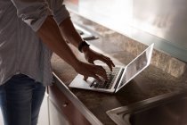 Seção média do homem usando laptop na cozinha em casa — Fotografia de Stock